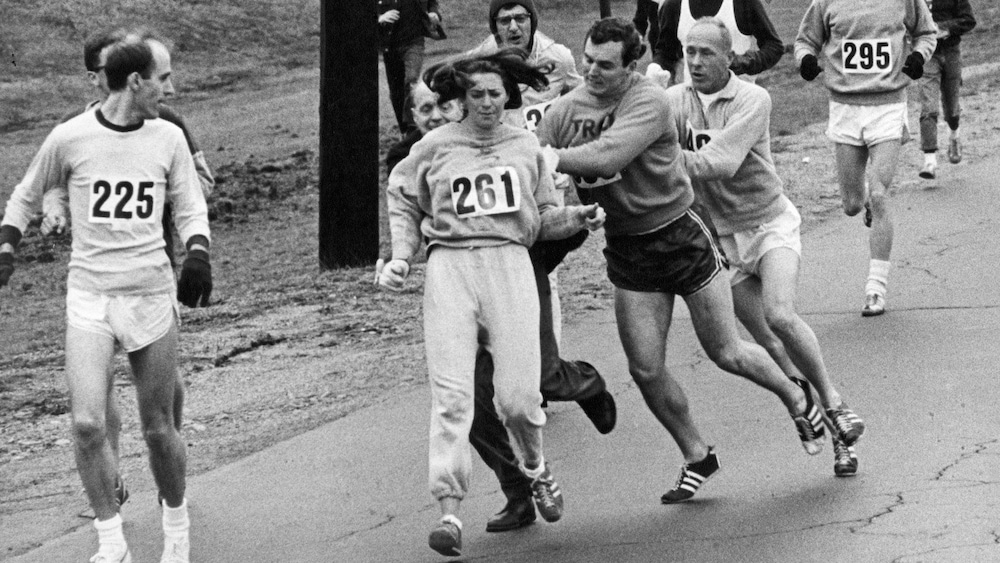 Tom Miller repousse Jock Semple (en noir) qui tente d'arracher son dossard à Kathrine Switzer lors du marathon de Boston en 1967.