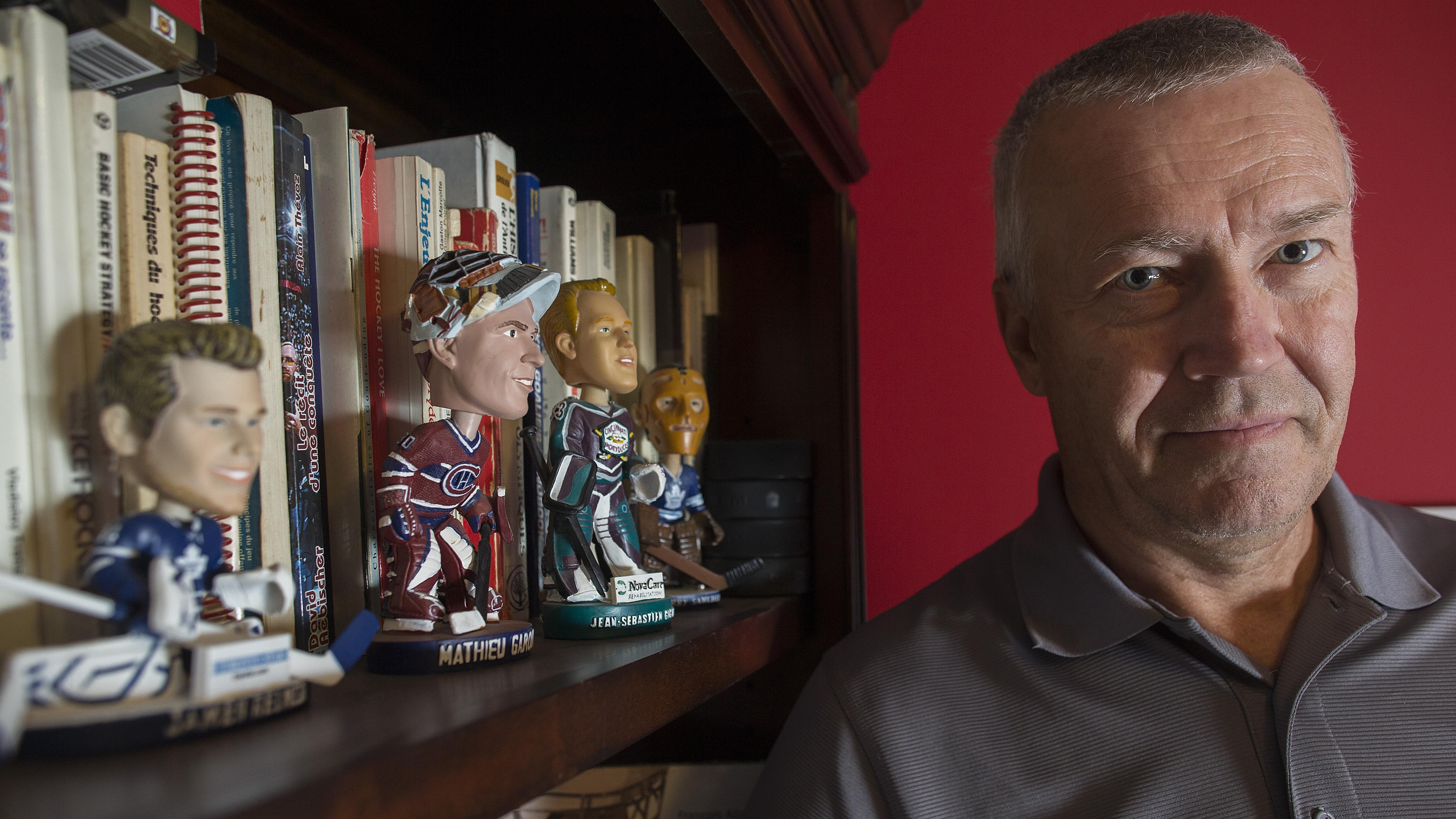 François Allaire se tient devant sa bibliothèque où se trouvent des figurines de gardiens de but