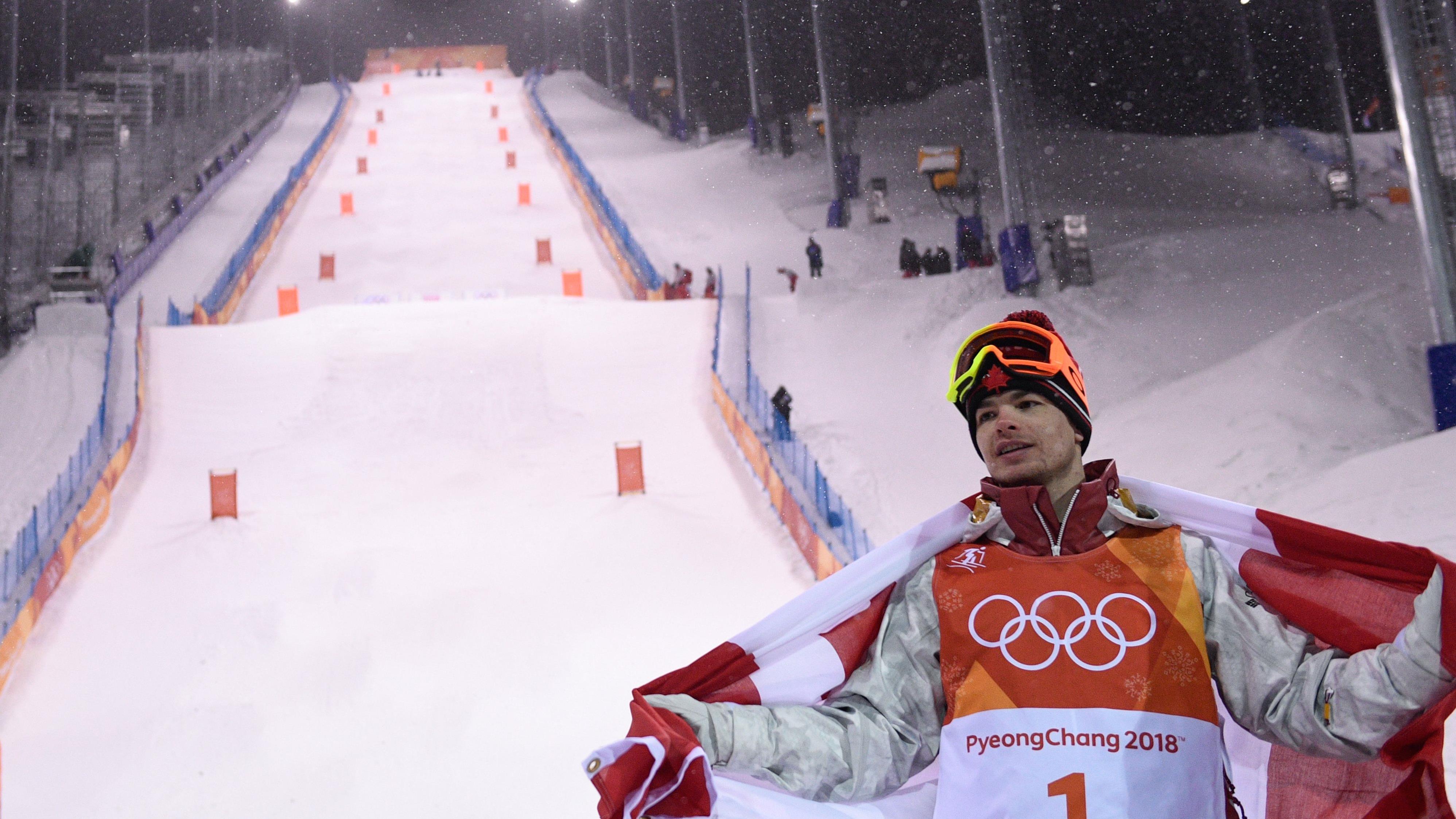 Mikaël Kingsbury se tient au pied de la pente olympique de bosses, de recouvrant du drapeau canadien.