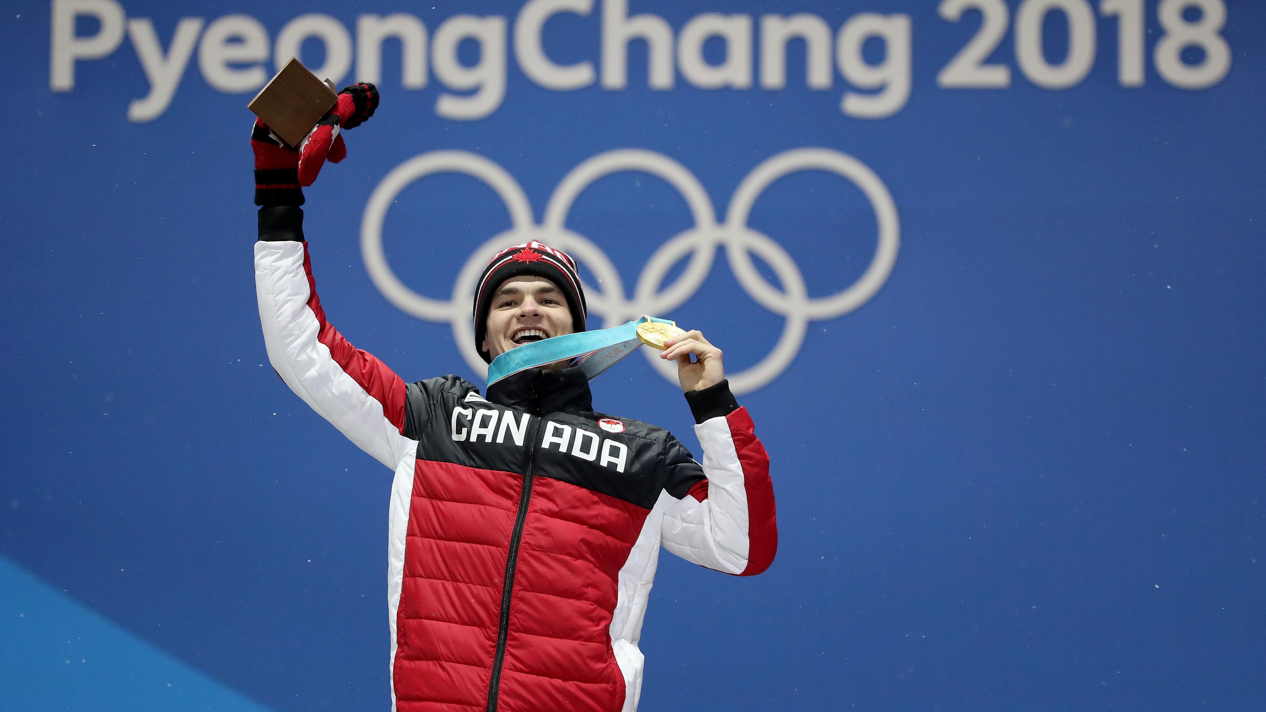 Mikaël Kingsbury tient sa médaille en signe de triomphe sur le podium.