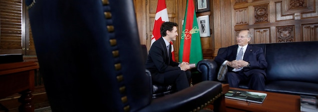Les deux hommes sont assis de biais sur de magnifiques divans dans un bâtiment du parlement canadien,