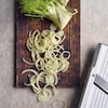 Du fenouil tranché sur une planche de bois et une mandoline en plastique.