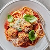 Des bucatinis dans une assiette recouverts de boulettes farcies au fromage et de morceaux de courgette.