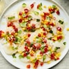 Un carpaccio de pétoncles garni de maïs, poivrons et coriandre dans une assiette.