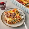 Un morceau de lasagne aux champignons, aux saucisses et aux rapinis dans une assiette avec une fourchette.