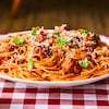 Une assiette de spaghetti aux boulettes sur une table avec une nappe à carreaux. 