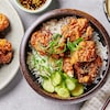 Des morceaux de poulet frit de style coréen, servis dans un bol avec du riz et des concombres marinés au gingembre.
