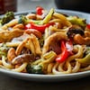 Sauté de nouilles udon au poulet effiloché dans une assiette.