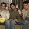 Les quatre personnages masculins de la série Les Invincibles assis sur un sofa, chacun brandit sa montre.