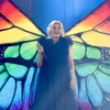L'animatrice porte de grandes ailes de papillon multicolores sur scène. 