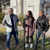 Trois personnes en conférence de presse devant une maison abandonnée.