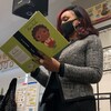 Jibs Abitoye, debout, lit un livre pour enfants dans une salle de classe. 