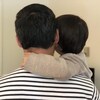 Un homme vu de dos tient son enfant dans ses bras. 
