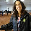 Caroline LeBlanc, psychologue et propriétaire du Serene View Ranch, debout devant son arène de chevaux où on voit un client à dos de cheval avec un assistant qui le guide.