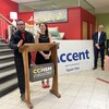 Deux personnes devant un lutrin, qui font une annonce. Derrière eux, une grosse pancarte avec le nom de l'entreprise.