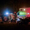 Des pompiers et des ambulanciers entourent le corps d'un homme, une moto est visible dans l'obscurité.