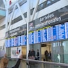Des tableaux d'affichage des arrivées internationales à l'aéroport Pearson sous lesquels des voyageurs passent la guérite avec leurs bagages.