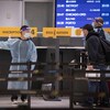 Des voyageurs font la file près d'un employé de l'aéroport portant un masque, une visière et une tenue protectrice.