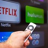 Une main tient une télécommande de télévision intelligente sur laquelle on voit les logos de plateformes de diffusion.