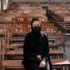 Une jeune Afghane vêtue d'une robe noire et d'un masque est assise sur un banc d'école.
