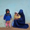 Une femme portant une burqa tient un enfant dans ses bras et se trouve près d'un autre.