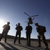 Cinq soldats américains attendent sur le tarmac pendant qu'un hélicoptère survole les lieux.