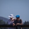 Un homme et une femme âgés penchés sur une balustrade en bois, par un temps chaud.