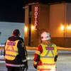 Un policier et un pompier de dos devant un hôtel. 