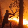 Un homme tente d'éteindre un incendie avec une branche.
