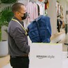 Une femme au comptoir d'un grand magasin de vêtements avec un employé et un sac portant le logo d'Amazon Style