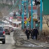 Un petit groupe de personnes marche sur un trottoir et des voitures circulent dans la rue.