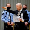 Entouré de policiers, Anders Breivik lève la main droite et tient une affiche qui demande de cesser le génocide des nations blanches.