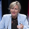 Andrée Laforest parle dans un micro lors d'une conférence de presse en tendant sa main gauche vers l'avant.