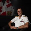 Angus Topshee pose en uniforme à côté de deux drapeaux de l'armée canadienne.