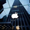 La devanture de la boutique d'Apple située au centre-ville de New York. La pomme illuminée orne un mur de verre, au travers duquel on aperçoit un gratte-ciel haut de dizaines d'étages.