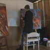 Une femme peint de dos dans une galerie.