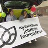 Deux jeunes femmes assises à l’arrière d’un véhicule montrent le logo de l’AJF durant le défilé.