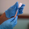 Un homme portant des gants extrait une dose d'un vaccin contre la COVID-19 d'une fiole.