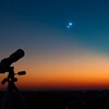 Un télescope au coucher du soleil avec deux planètes brillantes dans le ciel. 