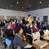 Environ 80 personnes sont assises sur des chaises dans une salle.