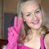 Une femme souriante avec des gants rose fait le signe de paix avec les doigts. 