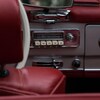 Dans une voiture ancienne, on voit l'appuie-tête rouge du siège en cuir et l'autoradio avec 5 gros boutons blancs.