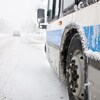 Un autobus circule sur une route enneigée. La visibilité est réduite par la brume et les précipitations de neige.