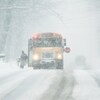 Un élève monte à bord d'un autobus scolaire pendant qu'il neige fortement.