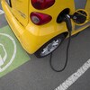 Une petite voiture électrique est rechargée dans un stationnement.