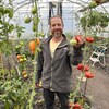 Éric Pineault sourit à la caméra en tenant une tomate, debout au milieu de sa serre.