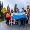 Des travailleurs et deux ministres sont debout sur la route et sourient en exhibant un drapeau du Labrador.