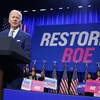 Joe Biden s'adresse à la foule devant une grande affiche où est inscrit Restore Roe. Plusieurs personnes tiennent des pancartes en faveur de du droit à l'avortement derrière lui. 