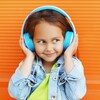 Une enfant écoute quelque chose qui la fait sourire avec des écouteurs bleus.