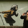 Une femme se prend en photo devant une murale de l'artiste de rue britannique Banksy illustrant une personne âgée qui éternue.